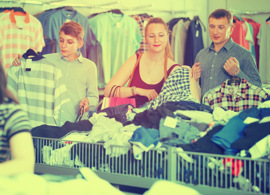 Positive family of three with teenager choosing clothes a half-off sale in the  shop