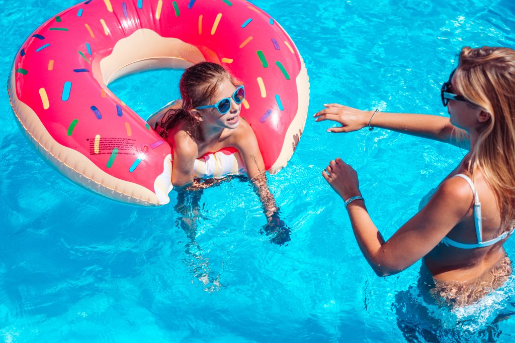 Little girl with her mom having fun in swimming pool.